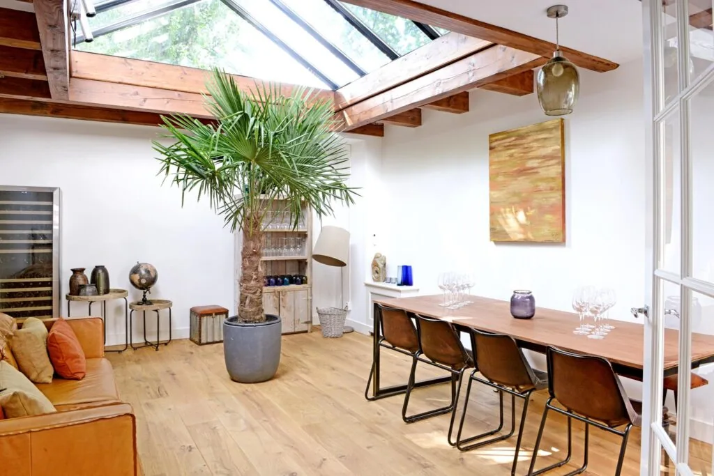 Lichte, modern ingerichte woonkamer aan de Nieuwe Kerkstraat met houten vloer, grote palmplant, dakraam en houten eettafel met stoelen.